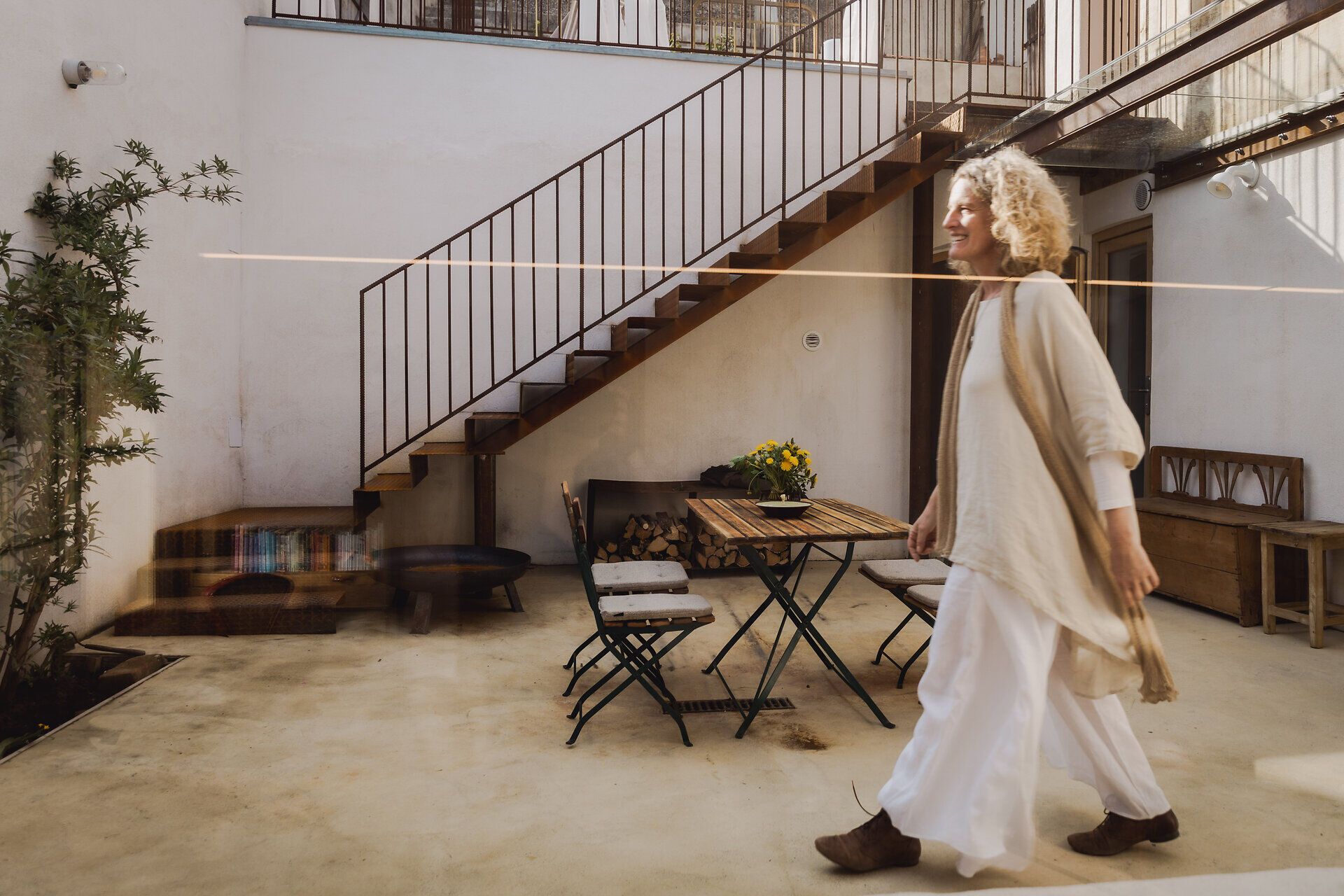 Innenhof mit Treppe und Sitzmöbeln, Frau im weißen Kleid geht vorbei.