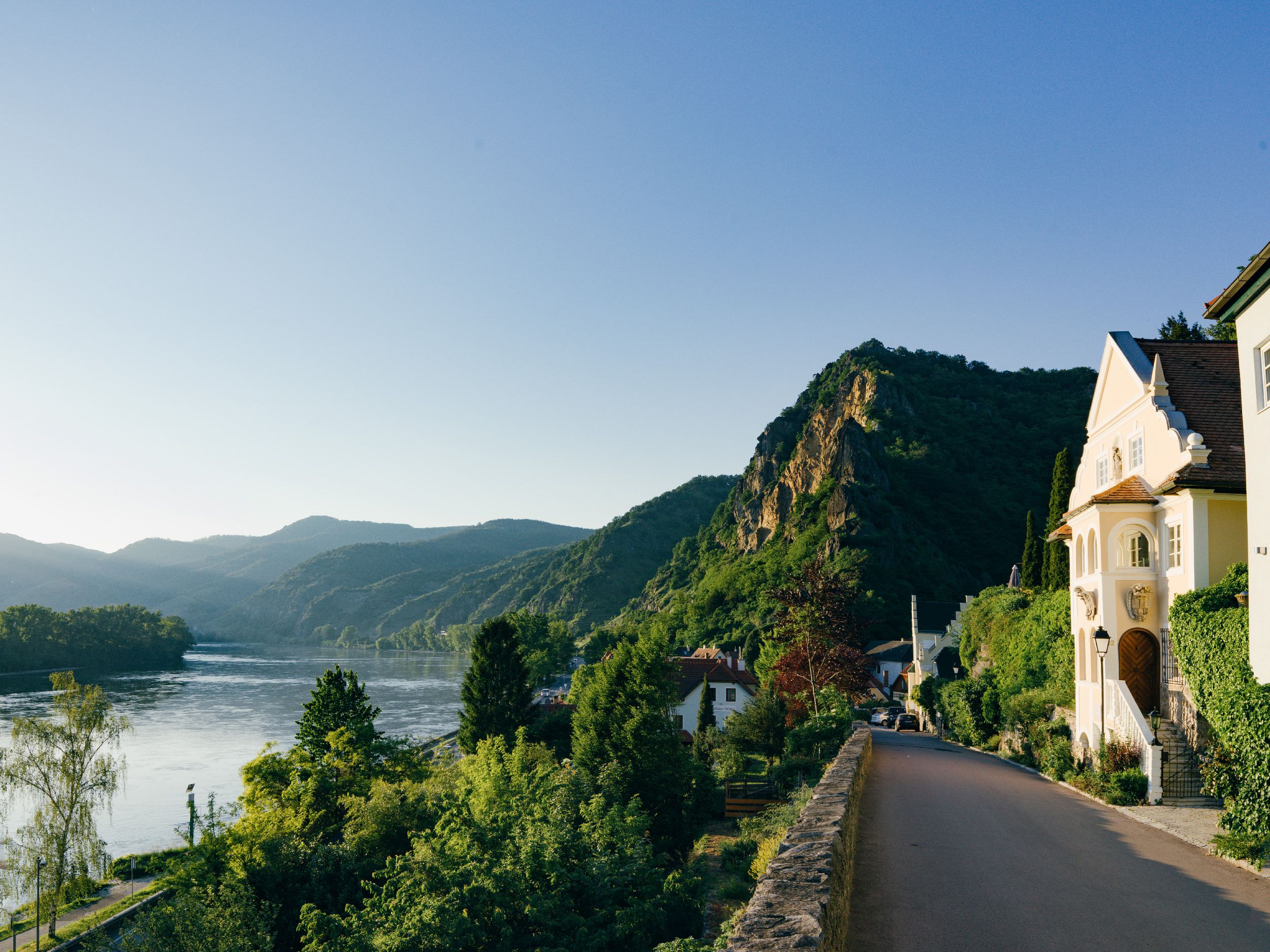 Landschaft mit Fluss, Bergen und Häusern bei Sonnenuntergang.