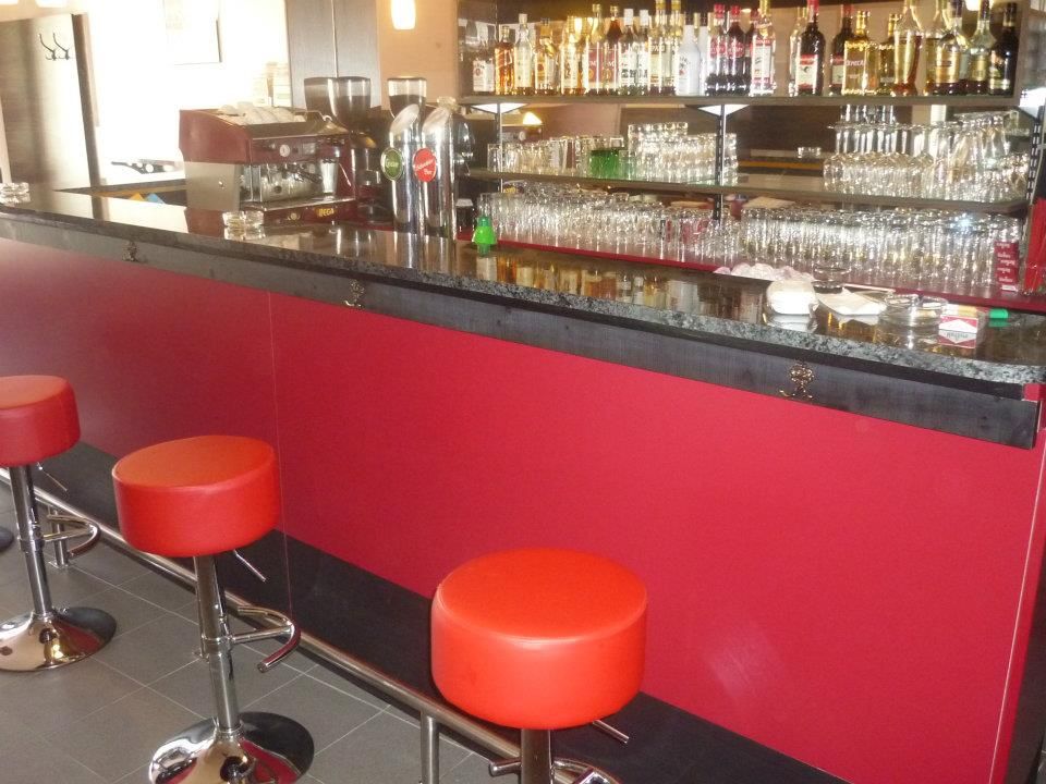 Innenansicht einer Bar mit roten Hockern und einer gut bestückten Theke.