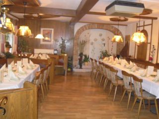 Ein gemütlicher Speiseraum mit langen, gedeckten Tischen und Holzstühlen, dekoriert mit Lampen und Pflanzen.