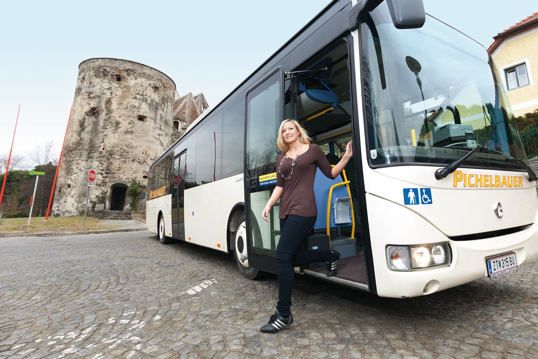 Eine Frau steigt aus einem Bus in der Wachau aus, im Hintergrund ein historischer Turm.