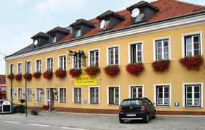 Gelbes Gebäude mit roten Blumen und Autos davor.
