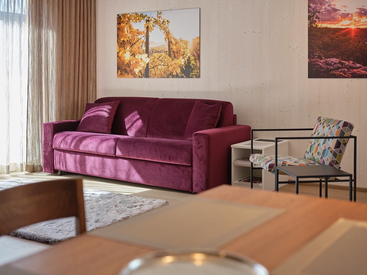 Wohnzimmer mit lila Sofa, buntem Stuhl und Wandbildern.