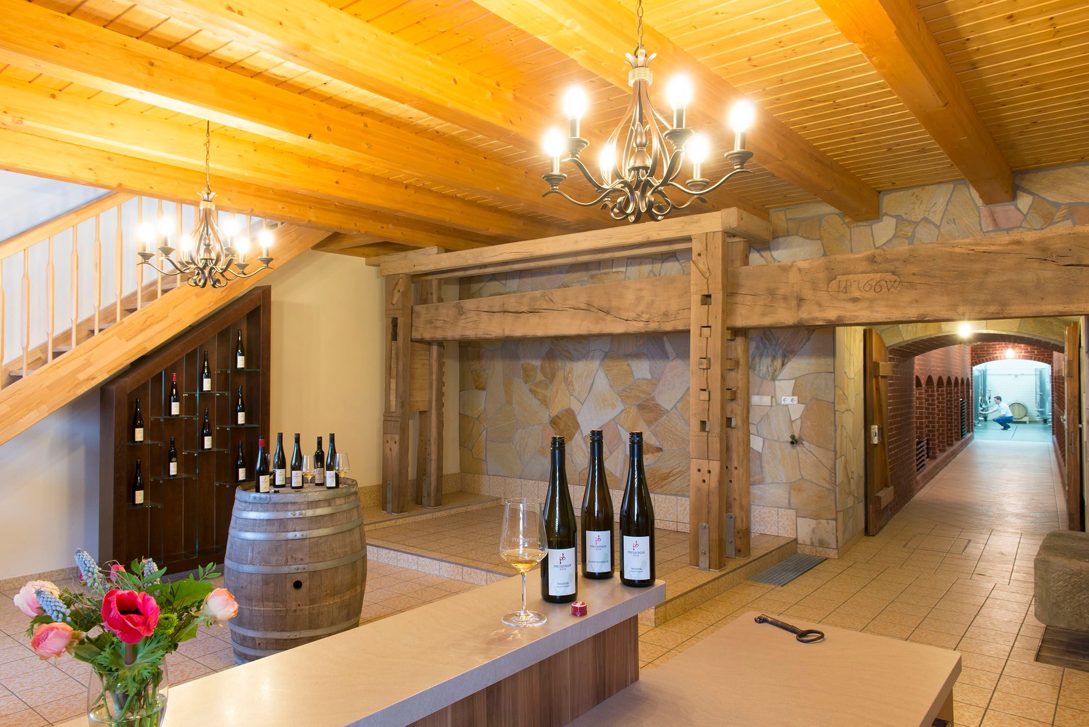 A tasting room with a wooden beamed ceiling, wine barrels and bottles on a barrel.