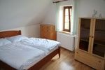 Ein Schlafzimmer mit einem Doppelbett, Holzkommode und Schrank, helle Wände und ein Fenster mit Vorhang.