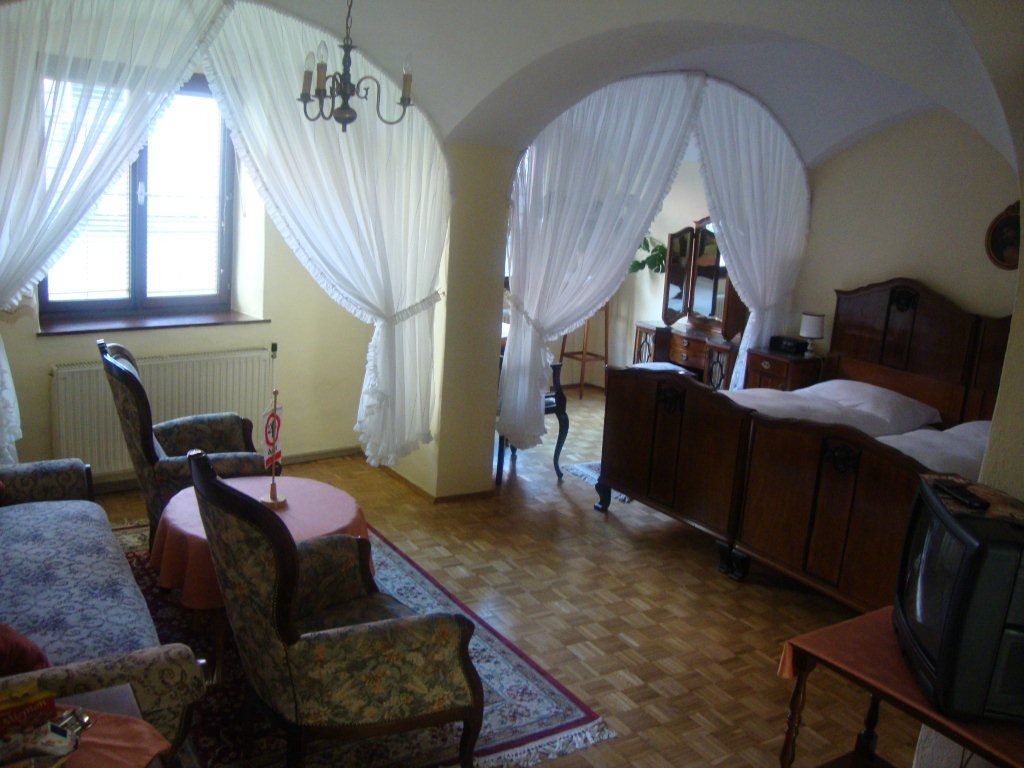 Ein gemütliches Gästezimmer mit antiken Möbeln, einem Doppelbett, Sesseln und einem kleinen Fernseher. Vorhänge trennen den Schlafbereich ab.