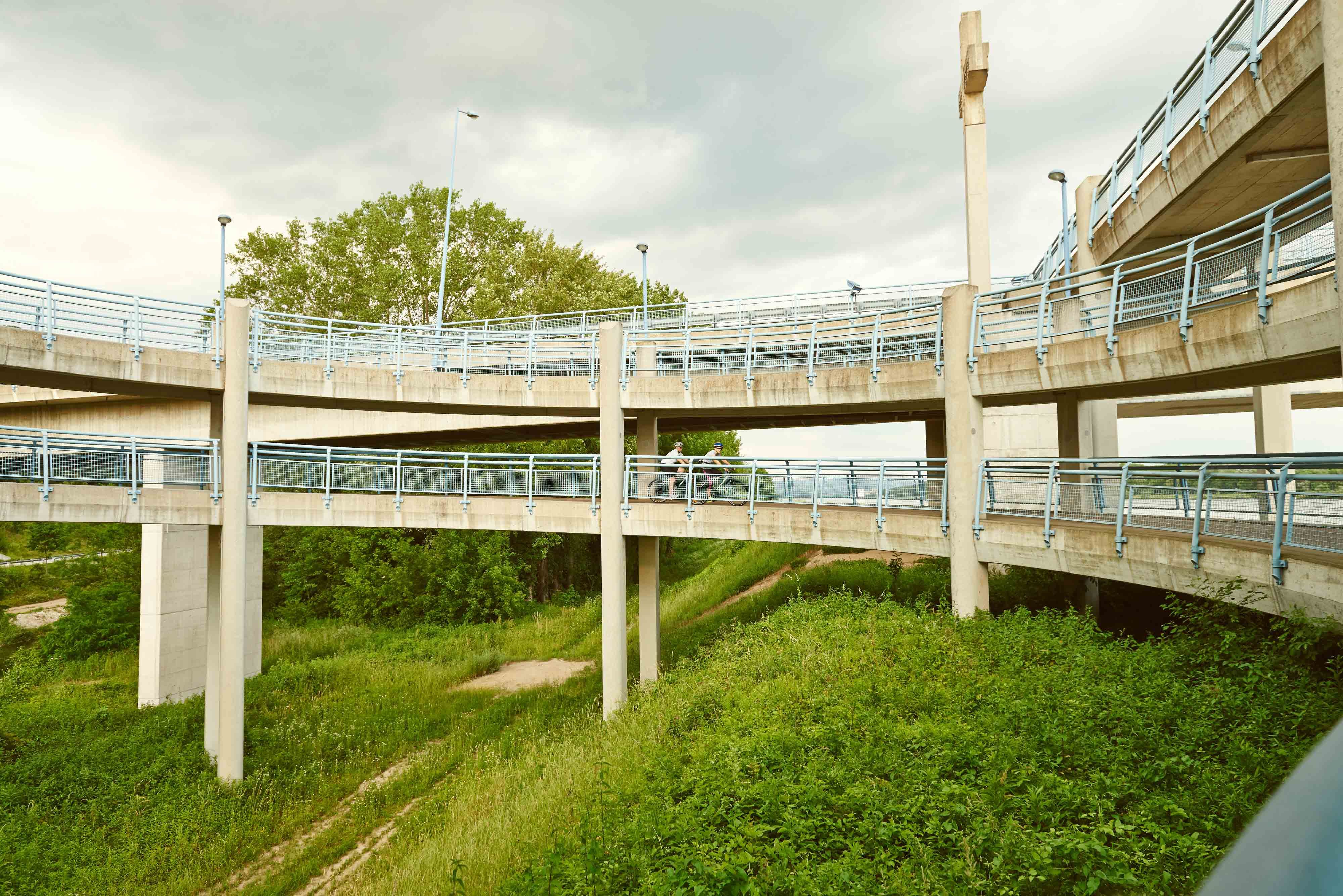 Eine mehrstöckige Fahrradrampe mit blauen Geländern in einer grünen Umgebung.
