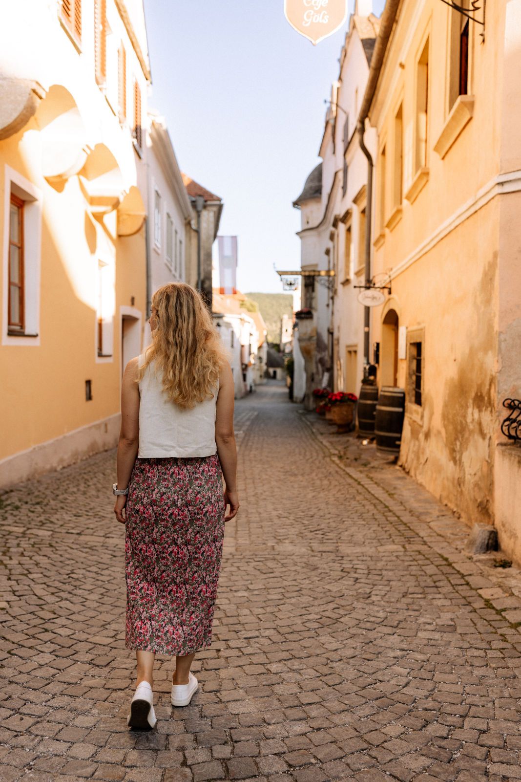 Eine Frau geht durch eine gepflasterte Gasse in Dürnstein, umgeben von historischen Gebäuden.