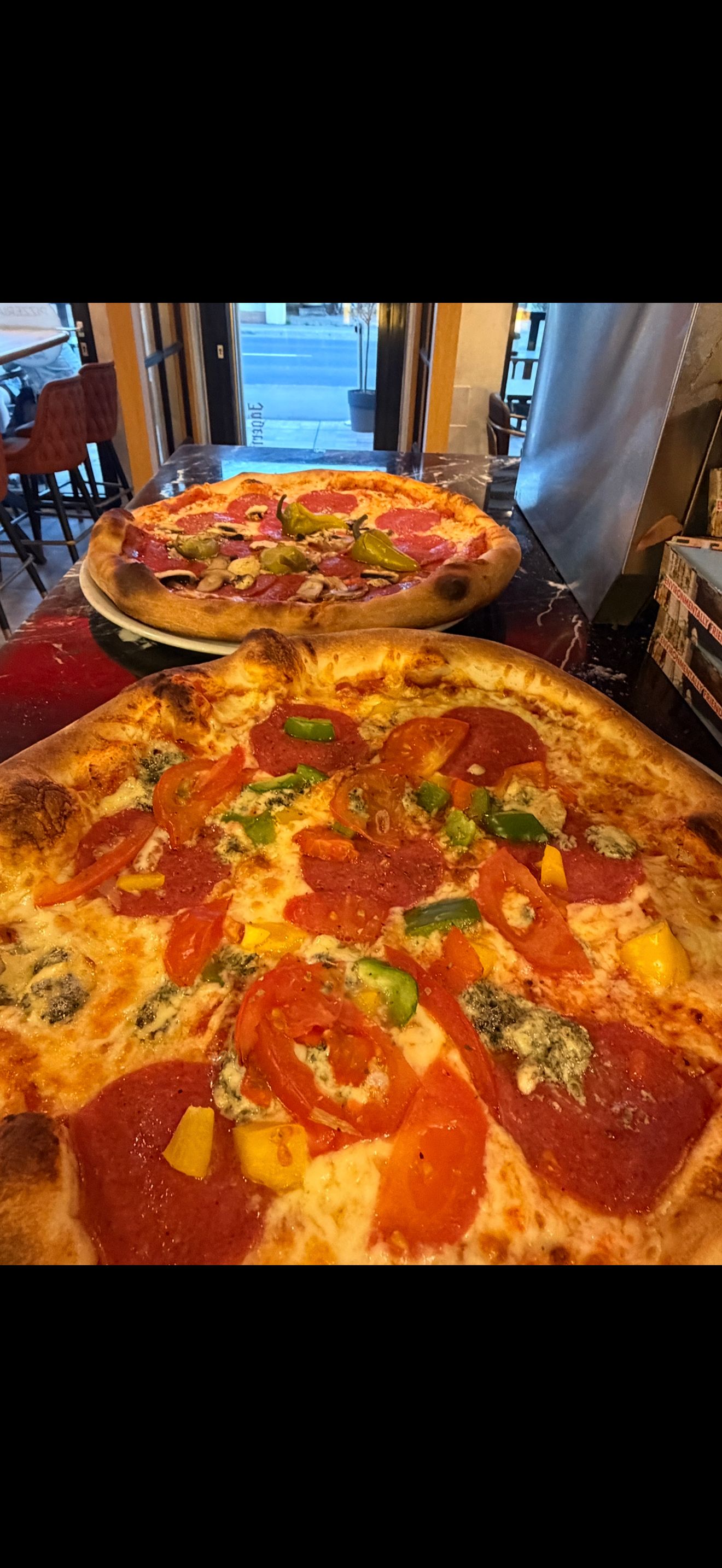Két pizza különböző feltétekkel egy pizzéria asztalán.