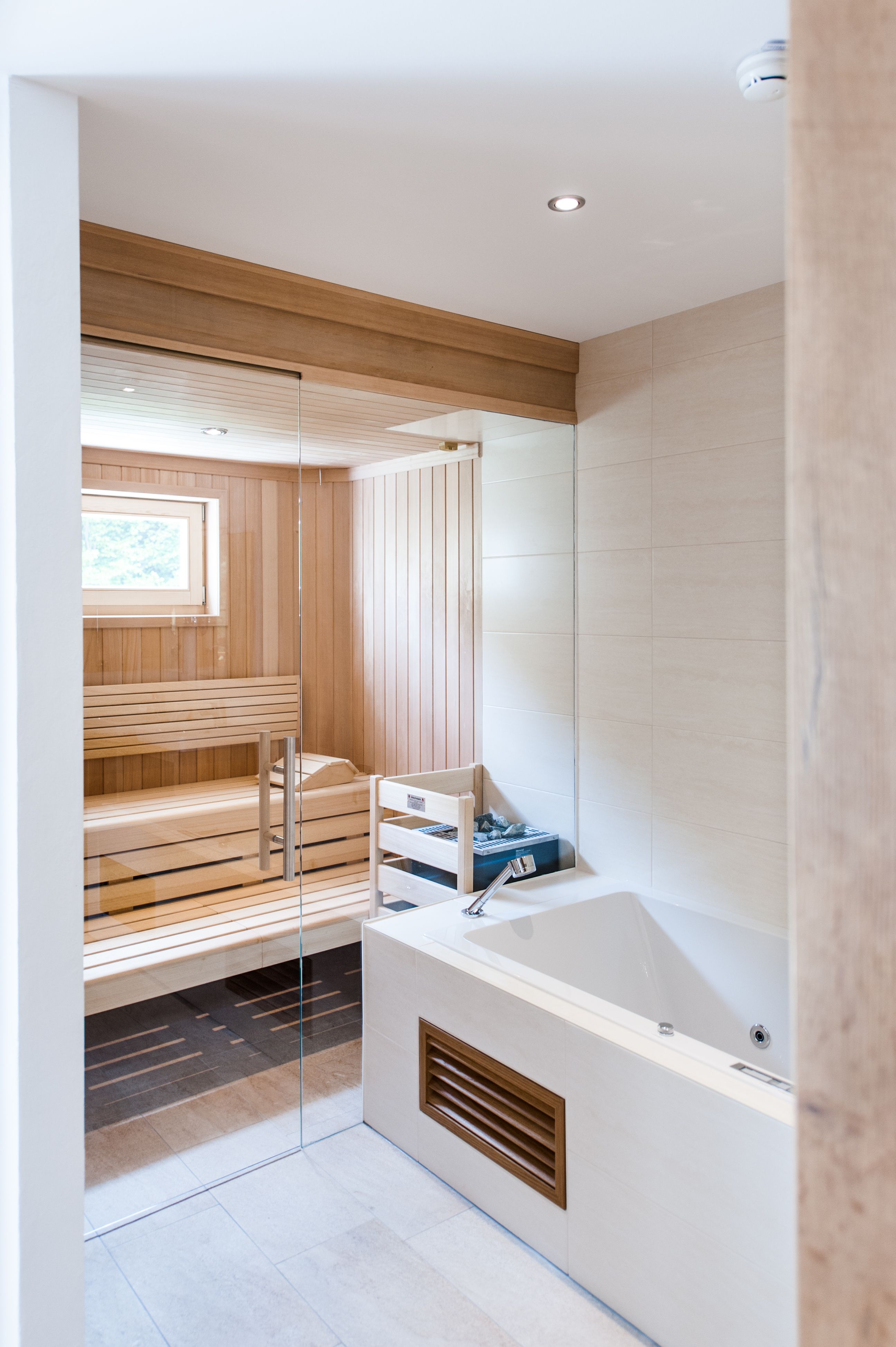 Innenansicht einer modernen Sauna mit Holzverkleidung und Glaswand, daneben eine weiße Badewanne.