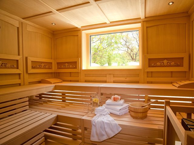 Innenansicht einer Sauna mit Holzbänken, Handtüchern und einem Fenster mit Blick ins Grüne.
