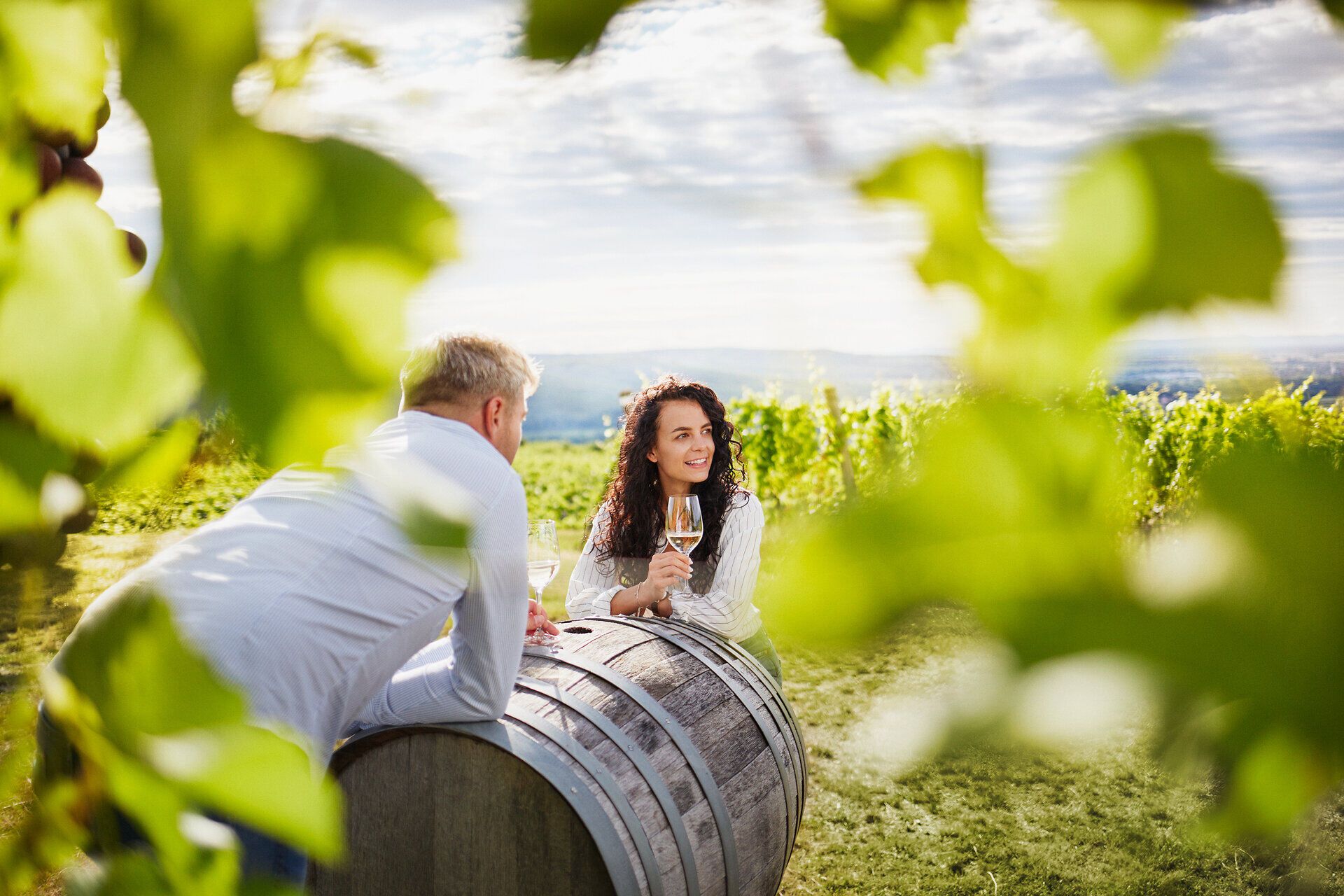 Inmitten der sanften Hügel des Kamptals genießen zwei Menschen ein Glas Wein und die atemberaubende Aussicht auf die Weinlandschaft. Die Sonne strahlt durch die Blätter der Reben und schafft eine einladende Atmosphäre, die zum Verweilen einlädt.
