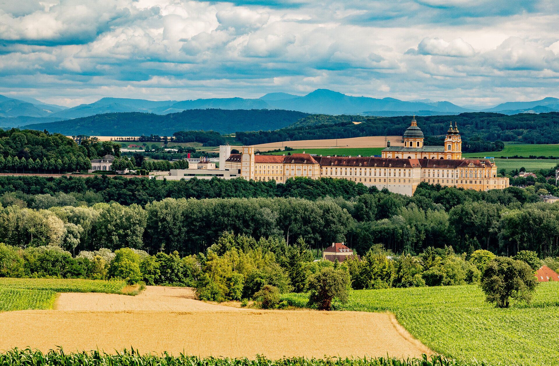 Umgeben von sanften Hügeln und üppigen Wäldern strahlt das majestätische Stift Melk eine zeitlose Ruhe aus. Die beeindruckende Architektur und die malerische Landschaft laden zu einem unvergesslichen Besuch ein, während die Wolken über den Bergen eine dramatische Kulisse schaffen.