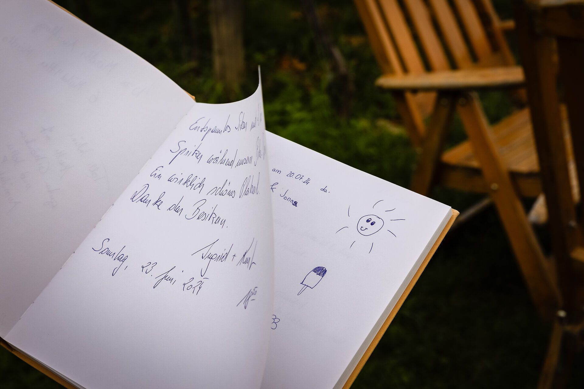 Ein gelbes Tagebuch in welchem Gäste handschriftlich Eindrücke hinterlassen, im Hintergrund ein Holz-Klappsessel.