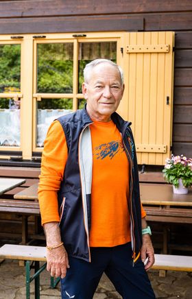 Mann steht vor einer Holzhütte mit Tischen und Bänken davor. 