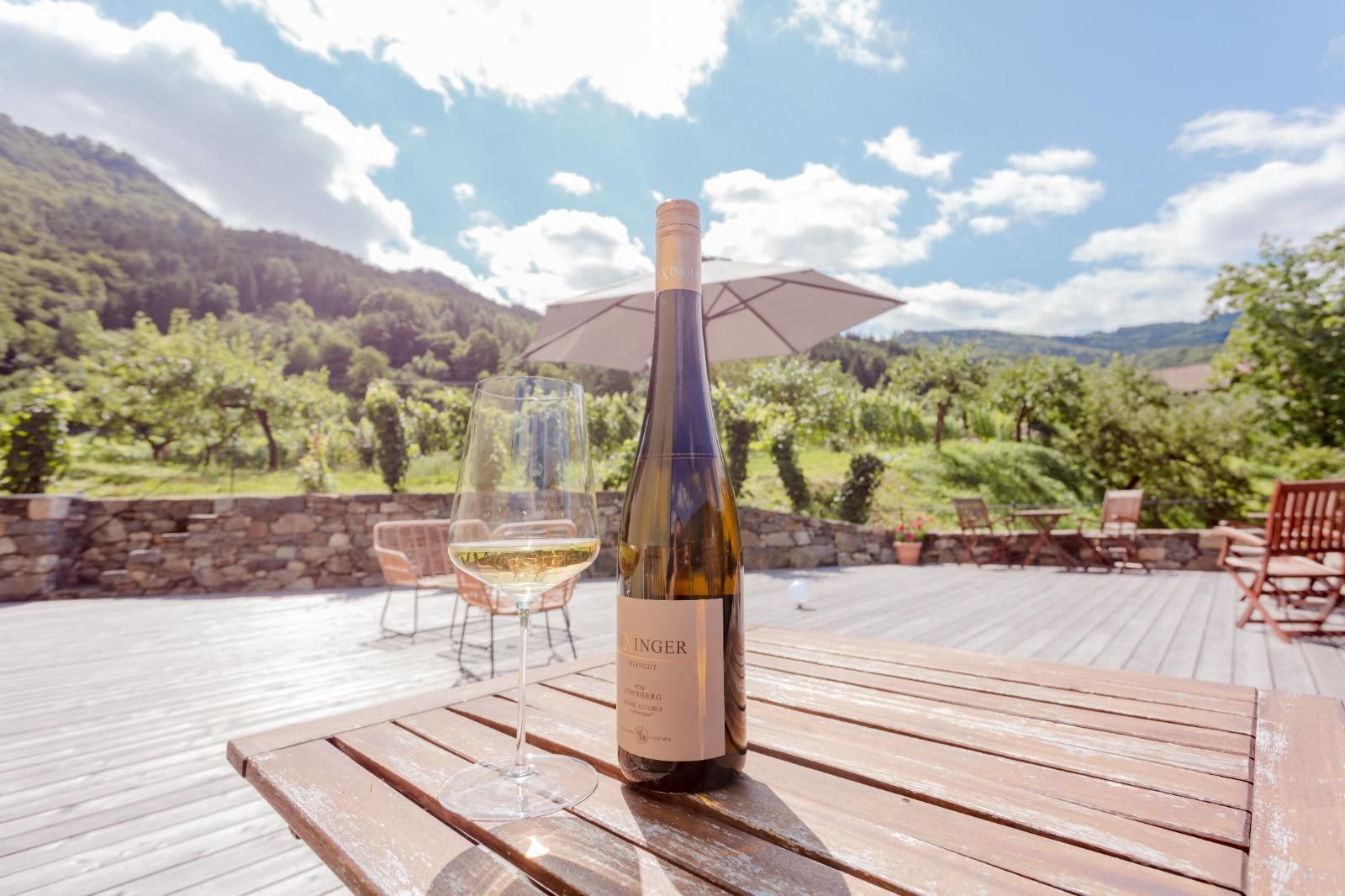 Weinflasche und Glas auf Holztisch mit Blick auf Weinberge und Berge.
