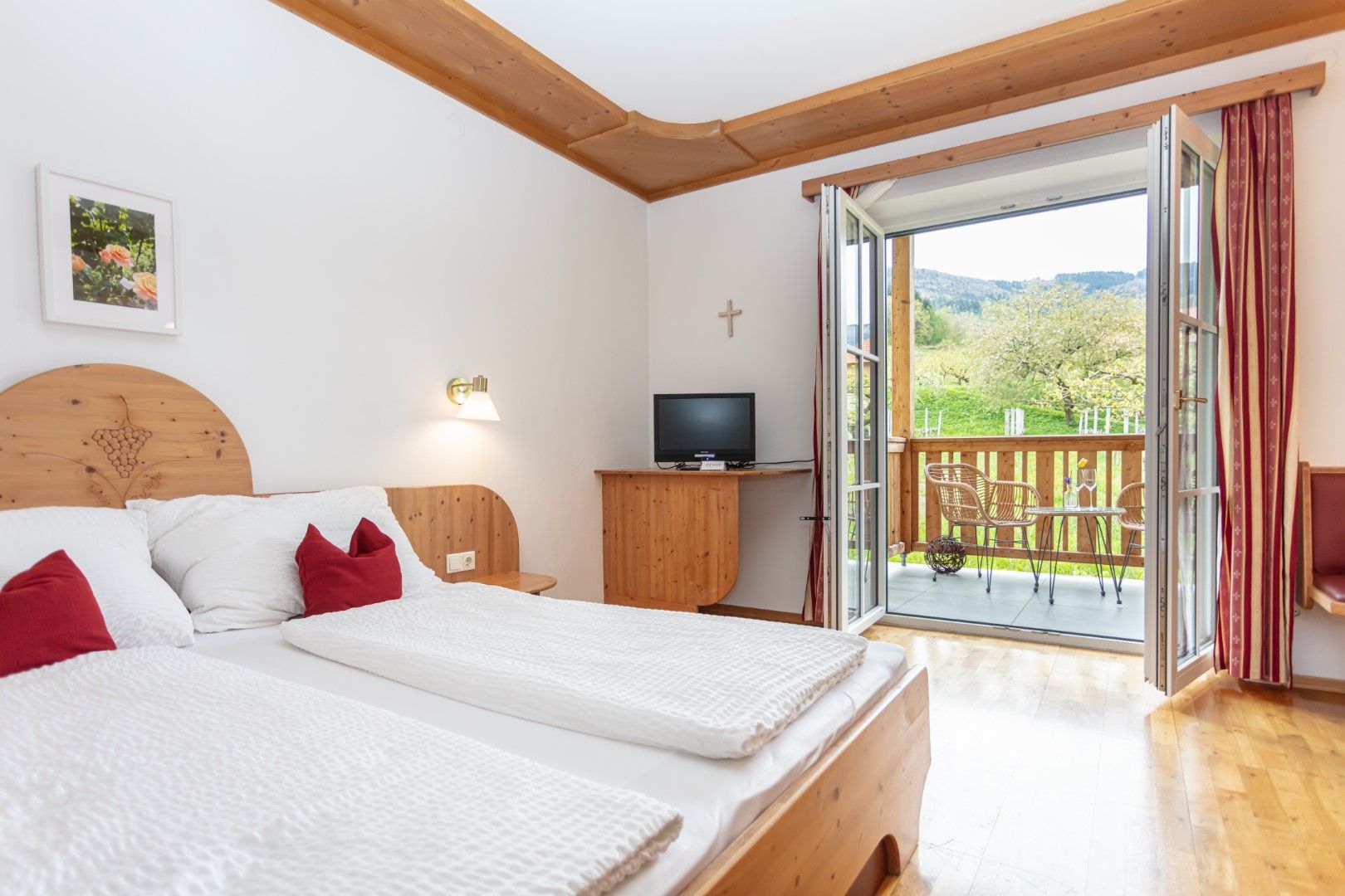Ein gemütliches Doppelzimmer mit Holzmöbeln, einem Balkon mit Blick ins Grüne und einem kleinen Fernseher.