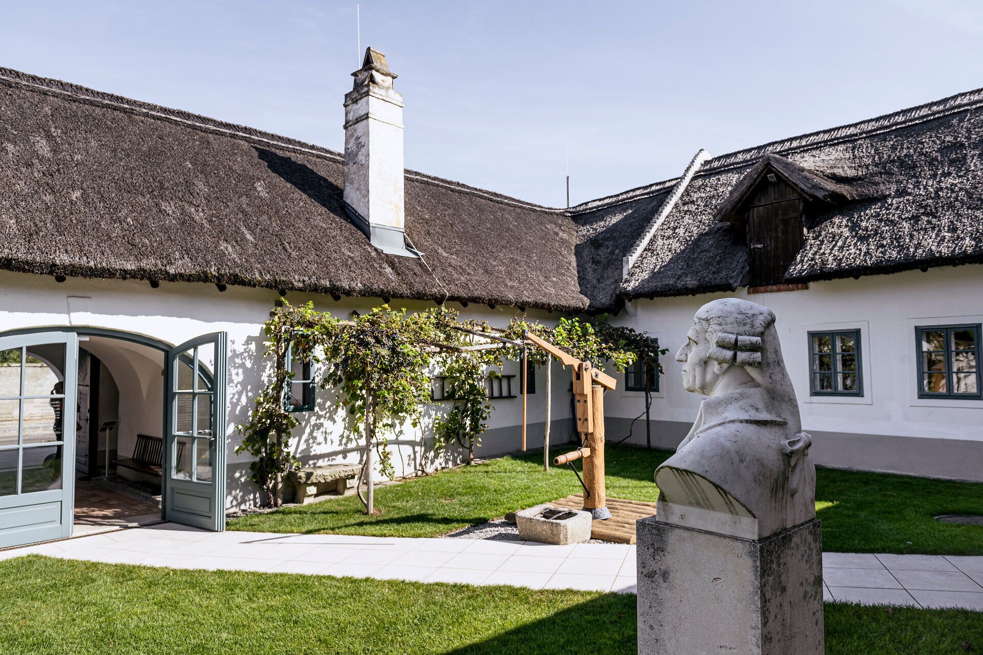 Innenhof des Haydn-Geburtshauses mit Strohdächern und einer Haydn-Büste.