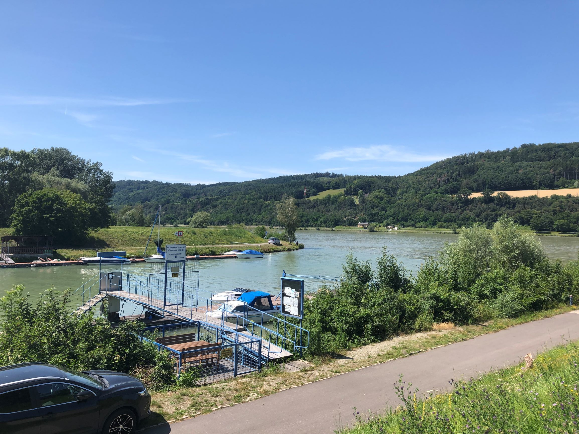 Anlegestelle am Fluss mit Booten und grüner Landschaft im Hintergrund.