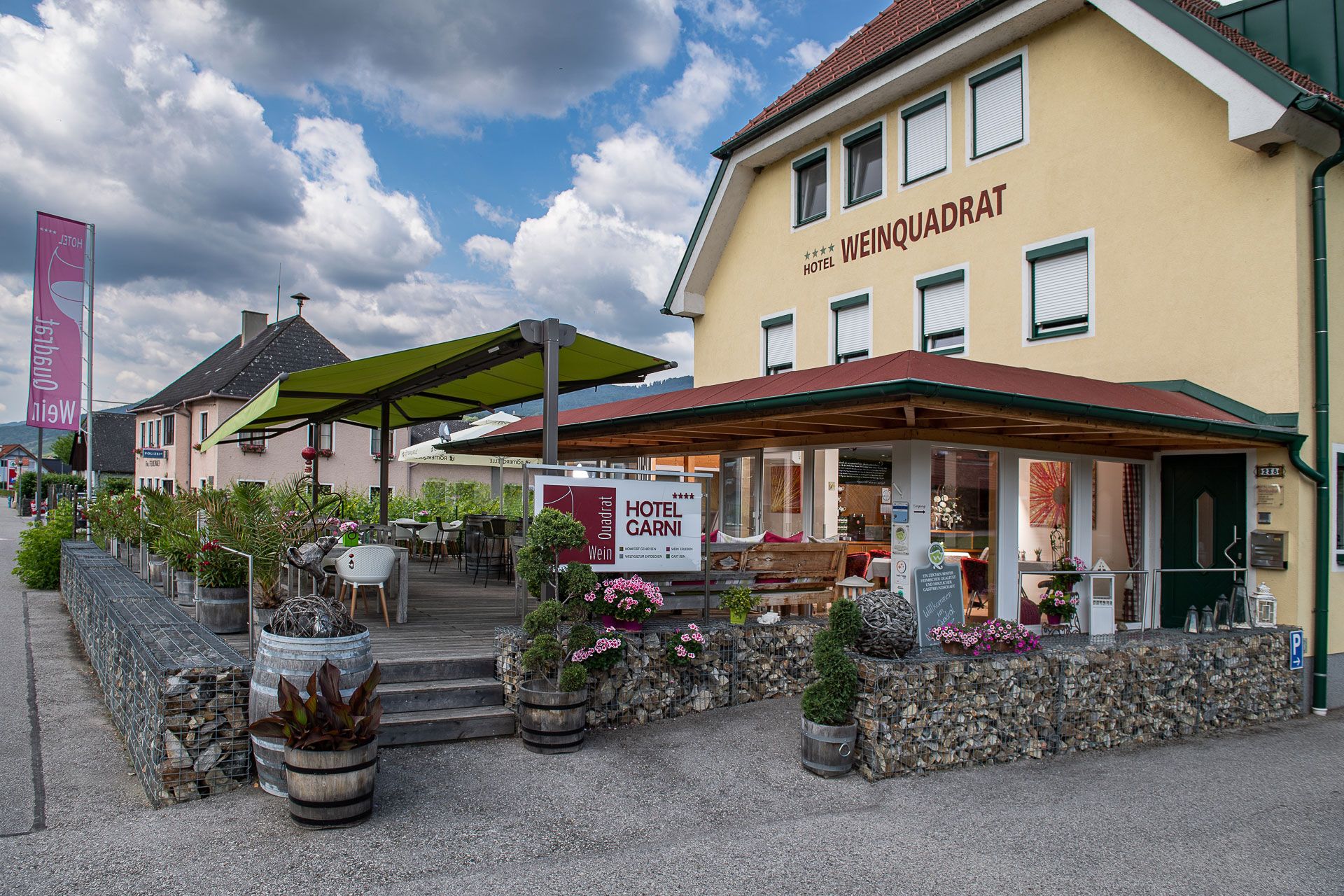 Außenansicht des Hotels Weinquadrat mit Terrasse und grünen Sonnenschirmen.