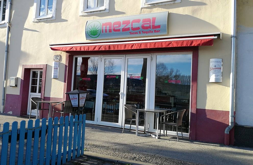 Außenansicht des Mezcal Restaurants mit roten Markisen und Sitzgelegenheiten.