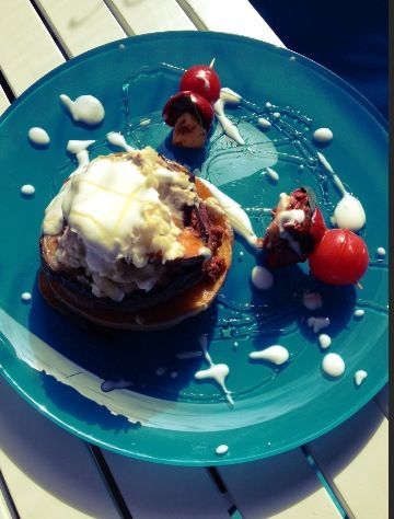 Ein blaues Teller mit einem Dessert, das aus Pancakes, Sahne und Kirschen besteht, auf einem Tisch.