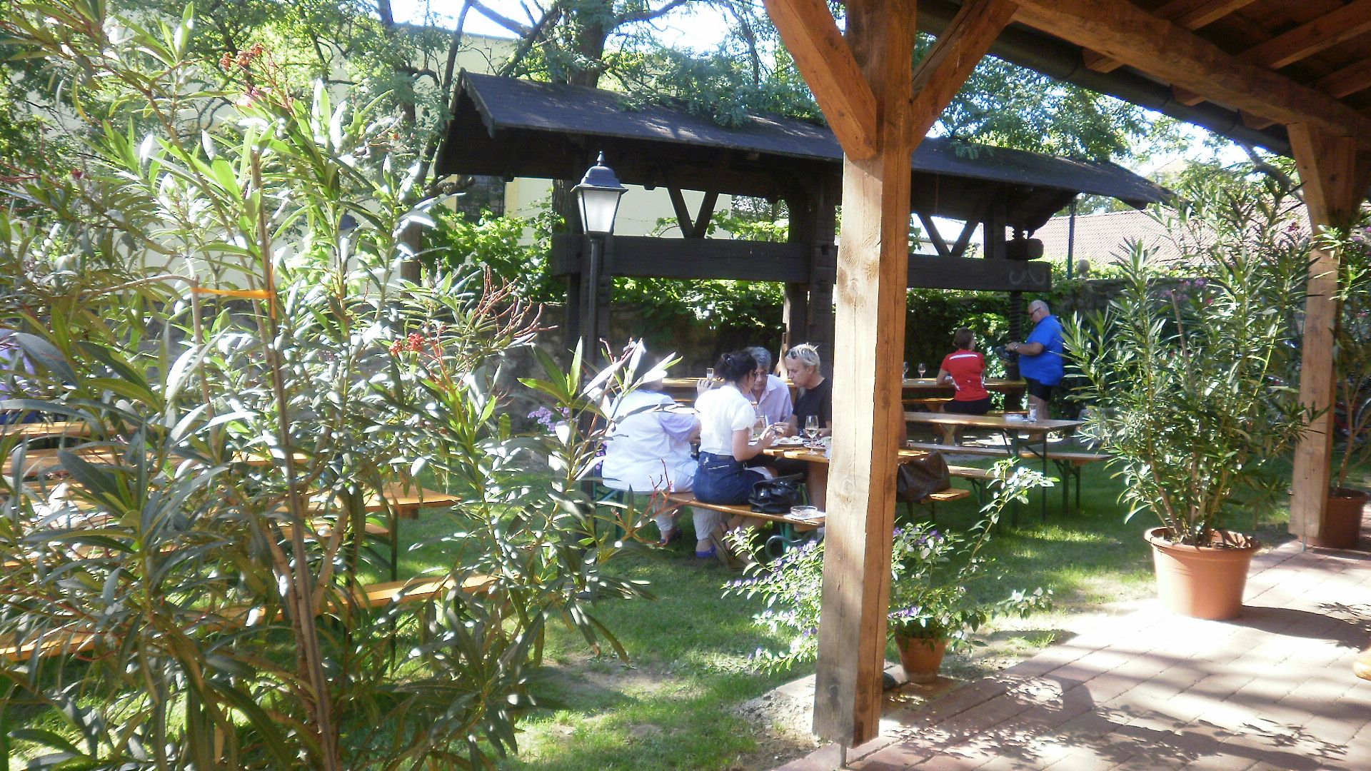 Garten eines Heurigenbetriebs mit Holztischen und Pflanzen.