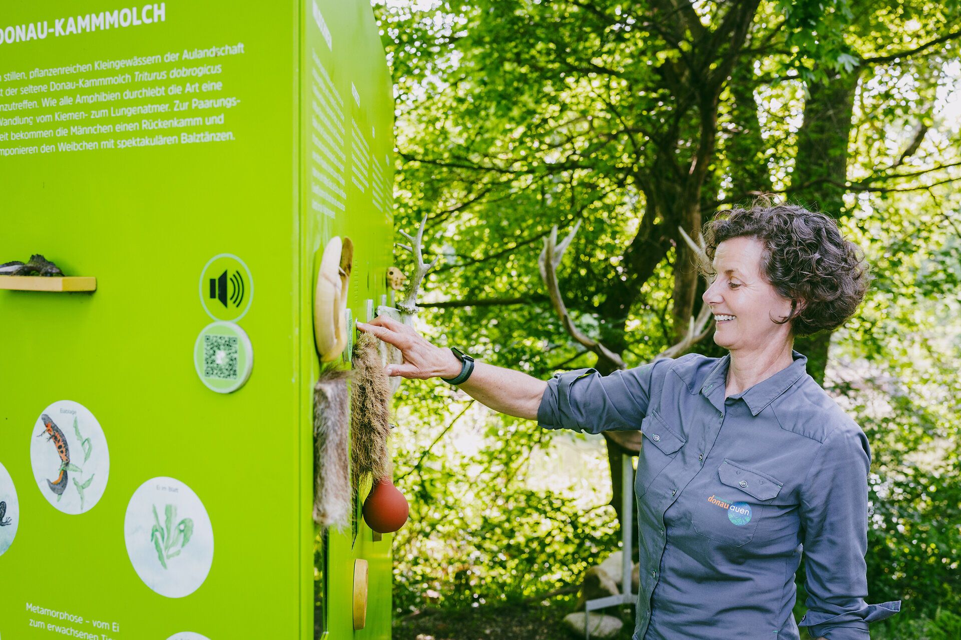 Nationalpark-Rangerin steht auf der Schlossinsel vor einer Schautafel mit tastbaren Objekten.