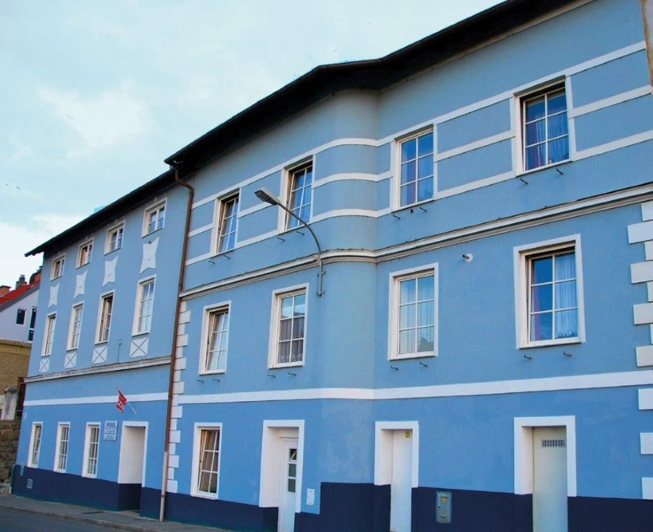 Blaue Fassade eines mehrstöckigen Gebäudes mit weißen Fensterrahmen und Türen.