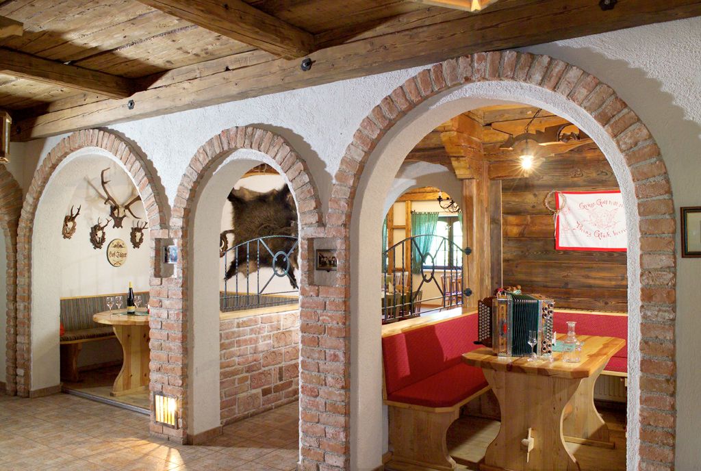 Rustikale Gaststube mit Holzmöbeln, Ziegelbögen und Jagdtrophäen an den Wänden.