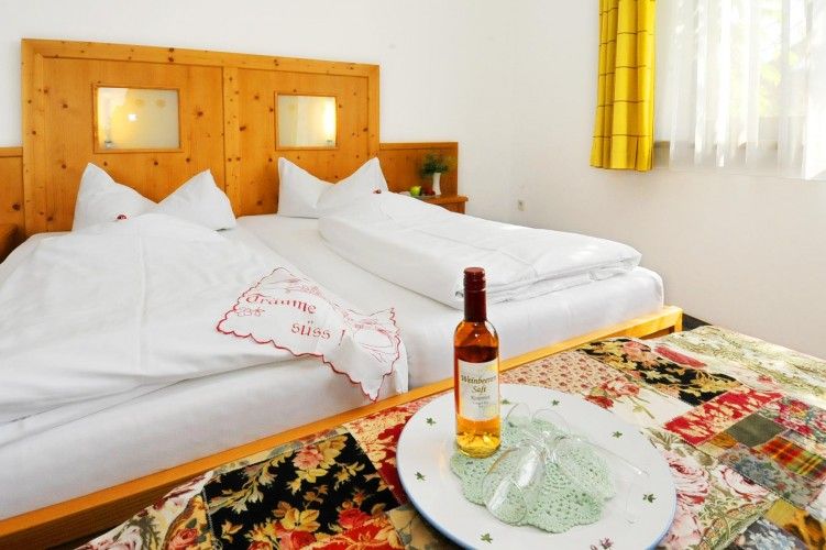 Cozy hotel room with double bed, decorated with an embroidered cushion and a bottle of wine on a table.