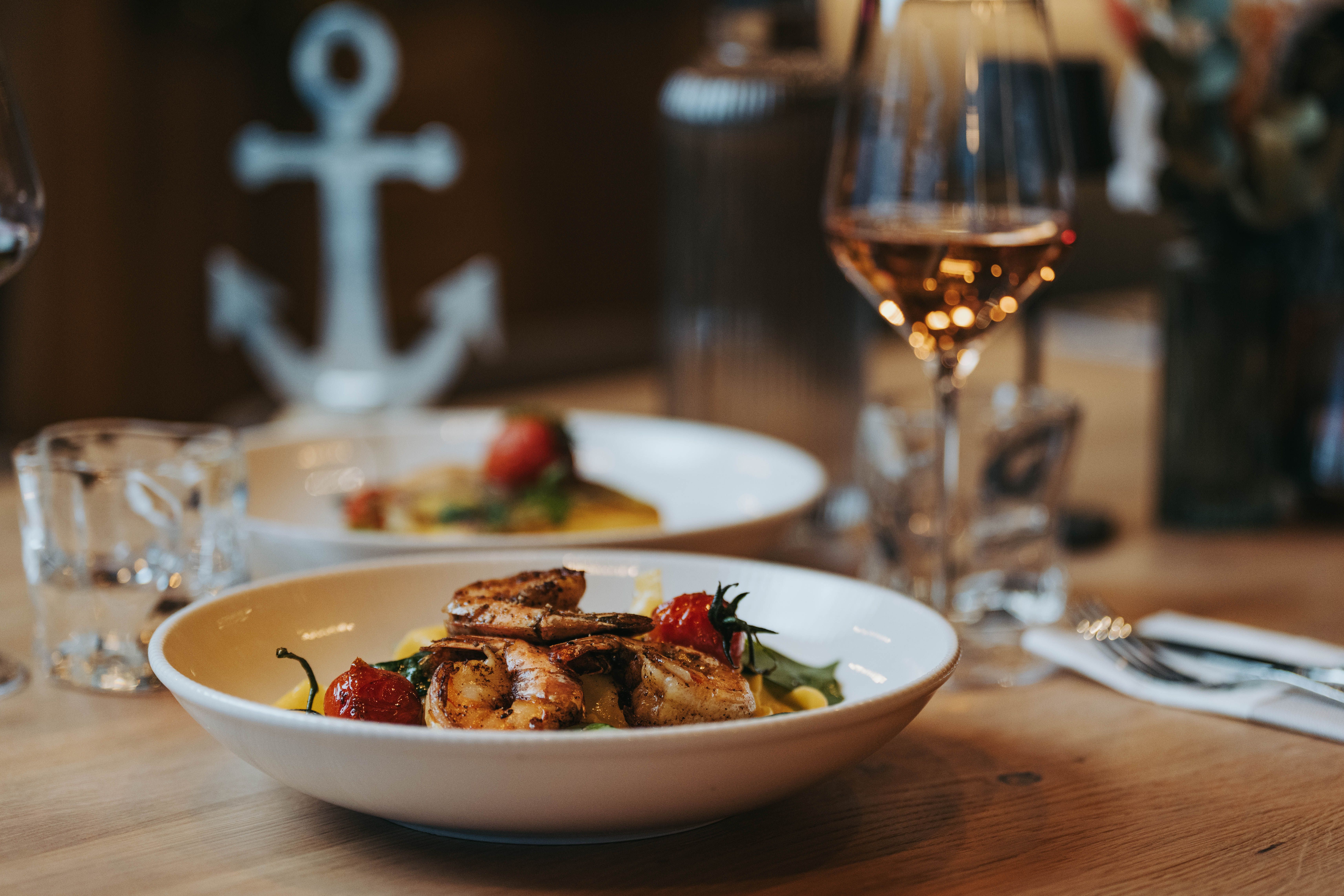 Ein Teller mit Garnelen und Gemüse auf einem Tisch, daneben ein Glas Wein.