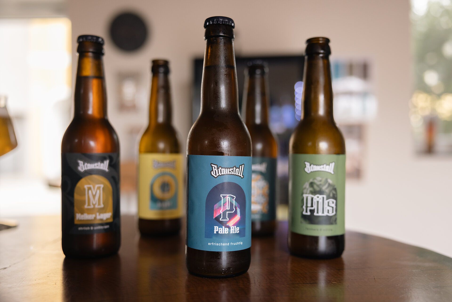 Mehrere Braustall-Bierflaschen verschiedener Sorten auf einem Holztisch, im Vordergrund eine Flasche Pale Ale.