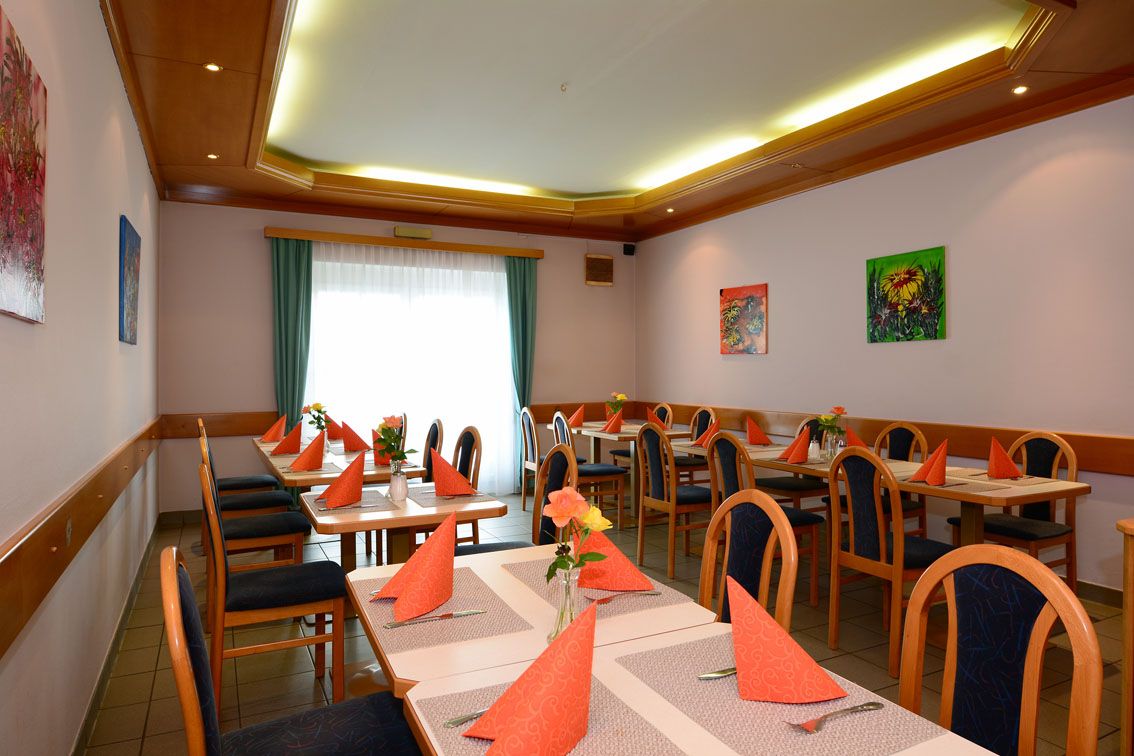 Ein Speisesaal mit gedeckten Tischen, orange Servietten und Blumenvasen.