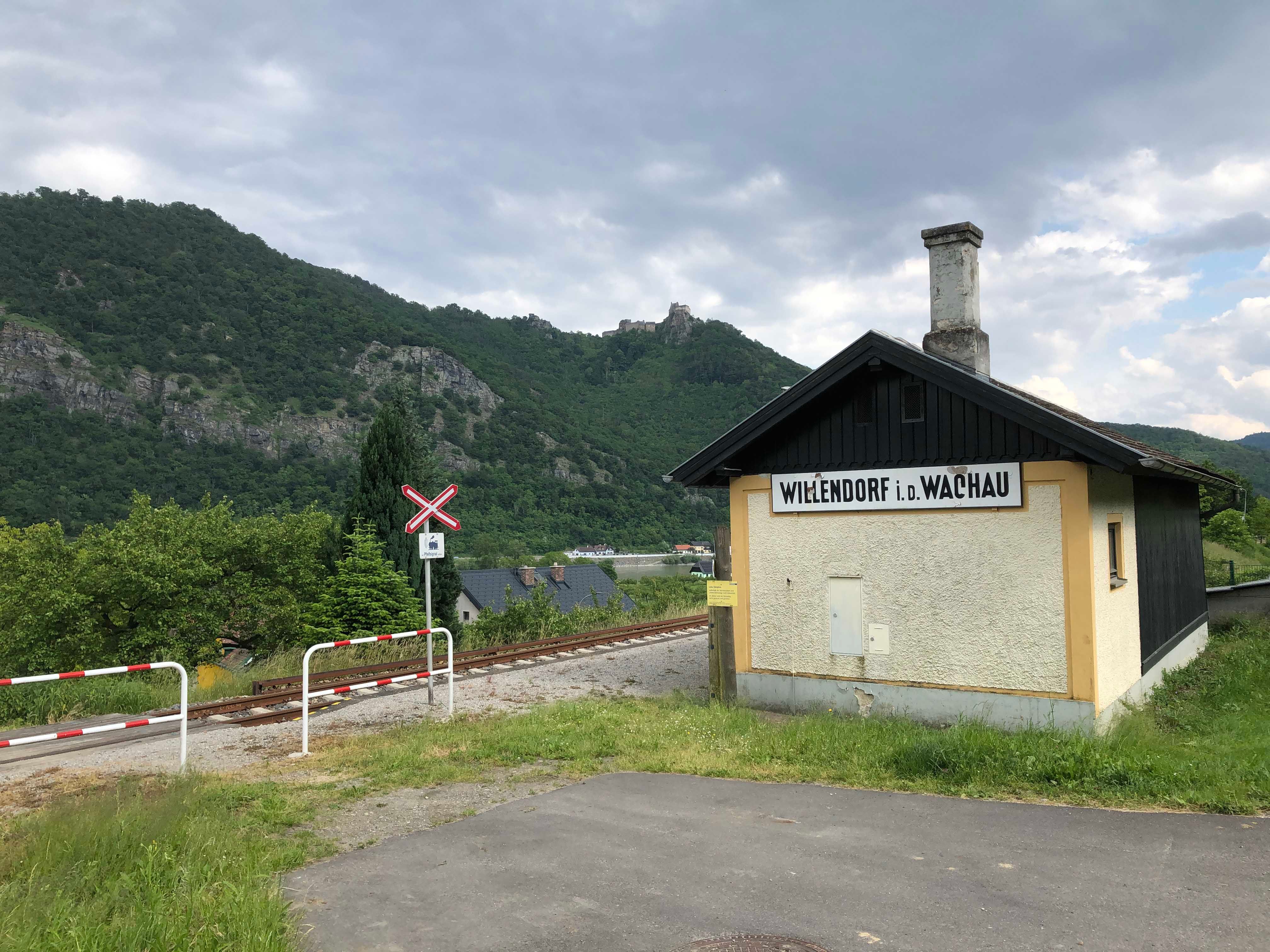 Kleines Bahnhofsgebäude in Willendorf in der Wachau, umgeben von grünen Hügeln und Bahngleisen.