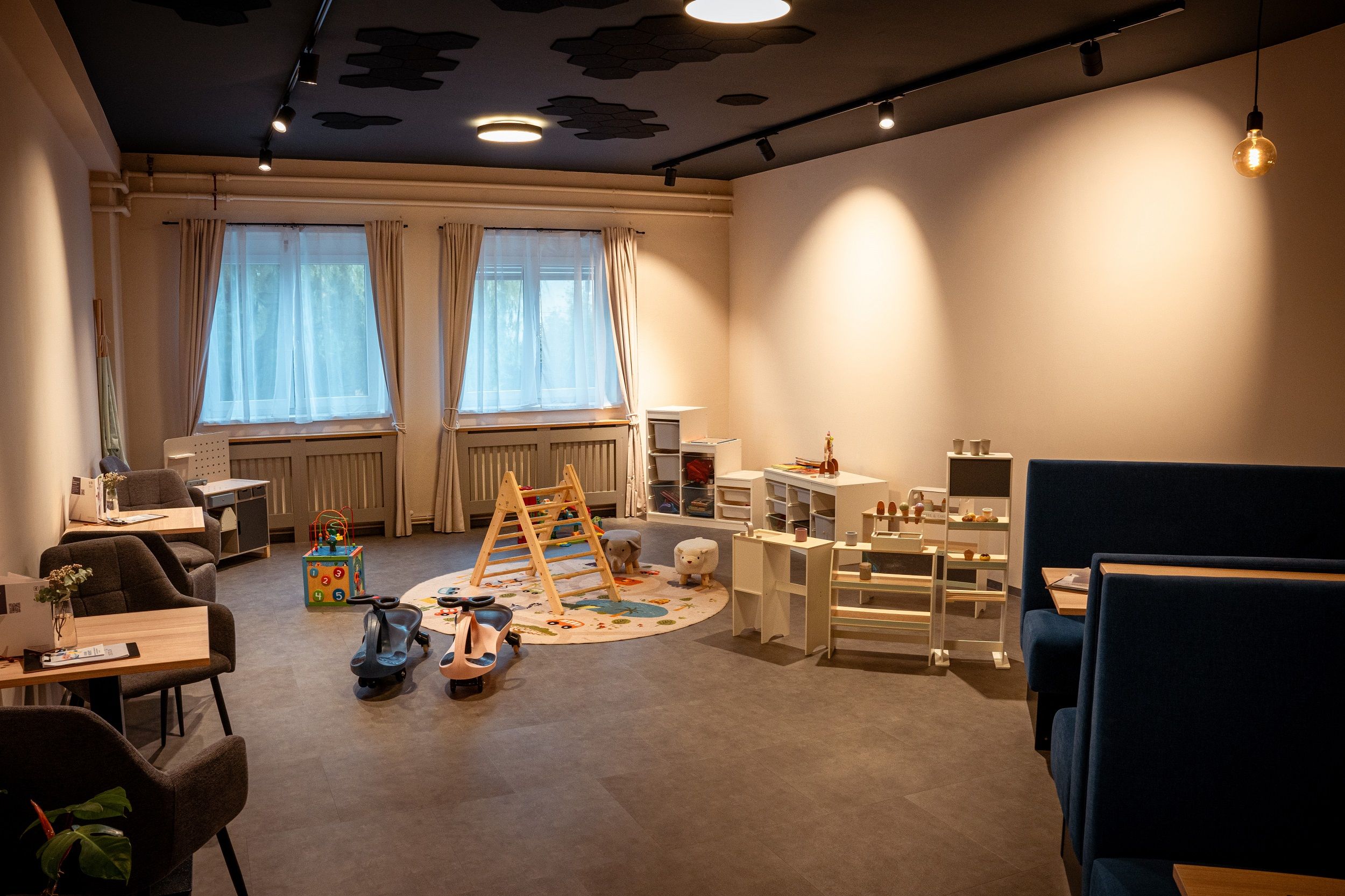 Spielzimmer für kleine Kinder mit SPielzeug am Boden, Tischen und einem Kaufmannsladen. 