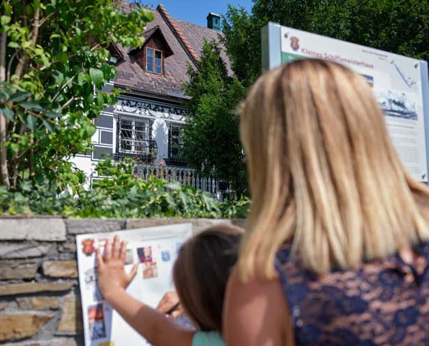 Egy nő és egy gyermek nézi az információs táblákat egy történelmi épület előtt.