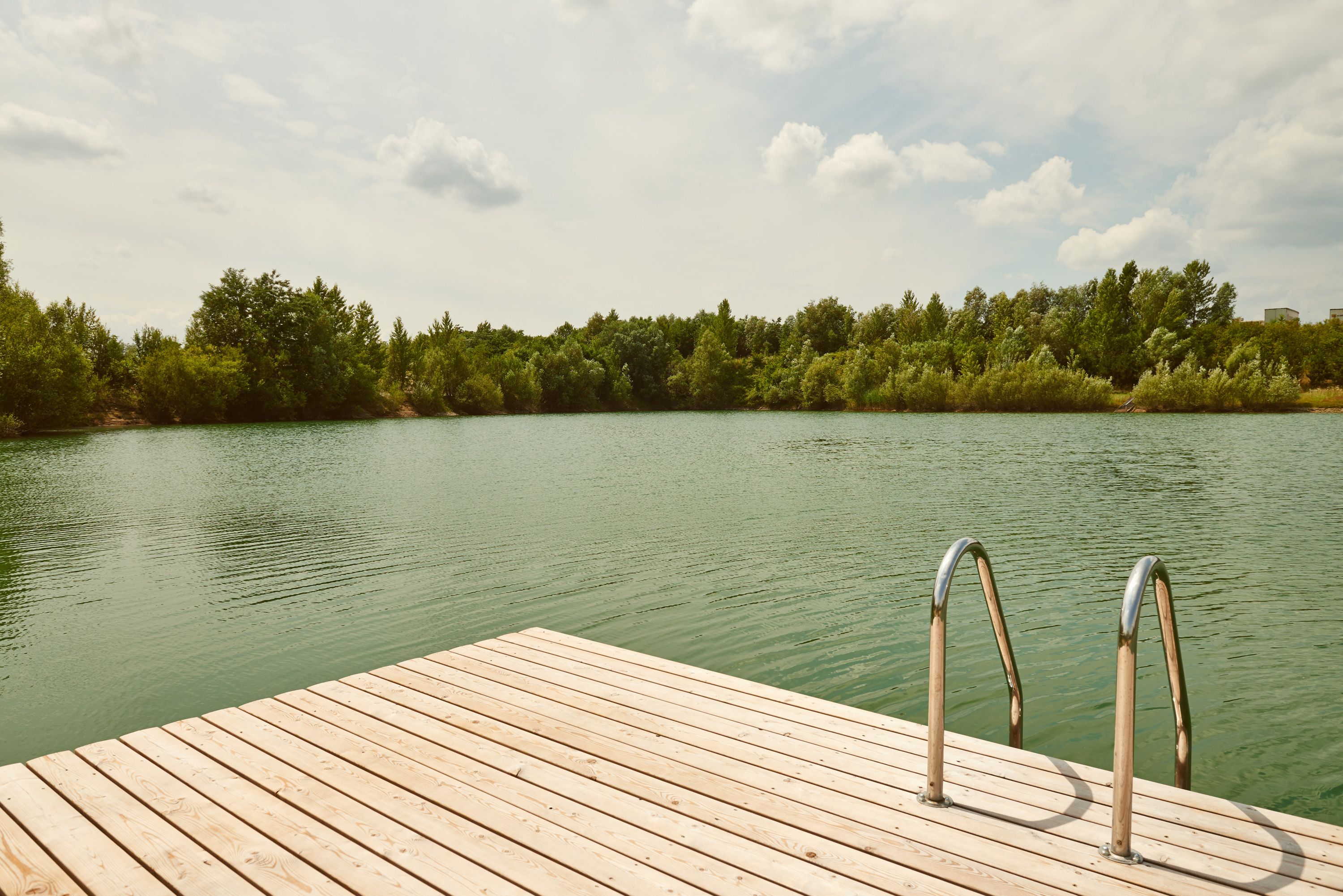 Holzsteg mit Leiter am Badeteich Persenbeug-Gottsdorf, umgeben von Bäumen.