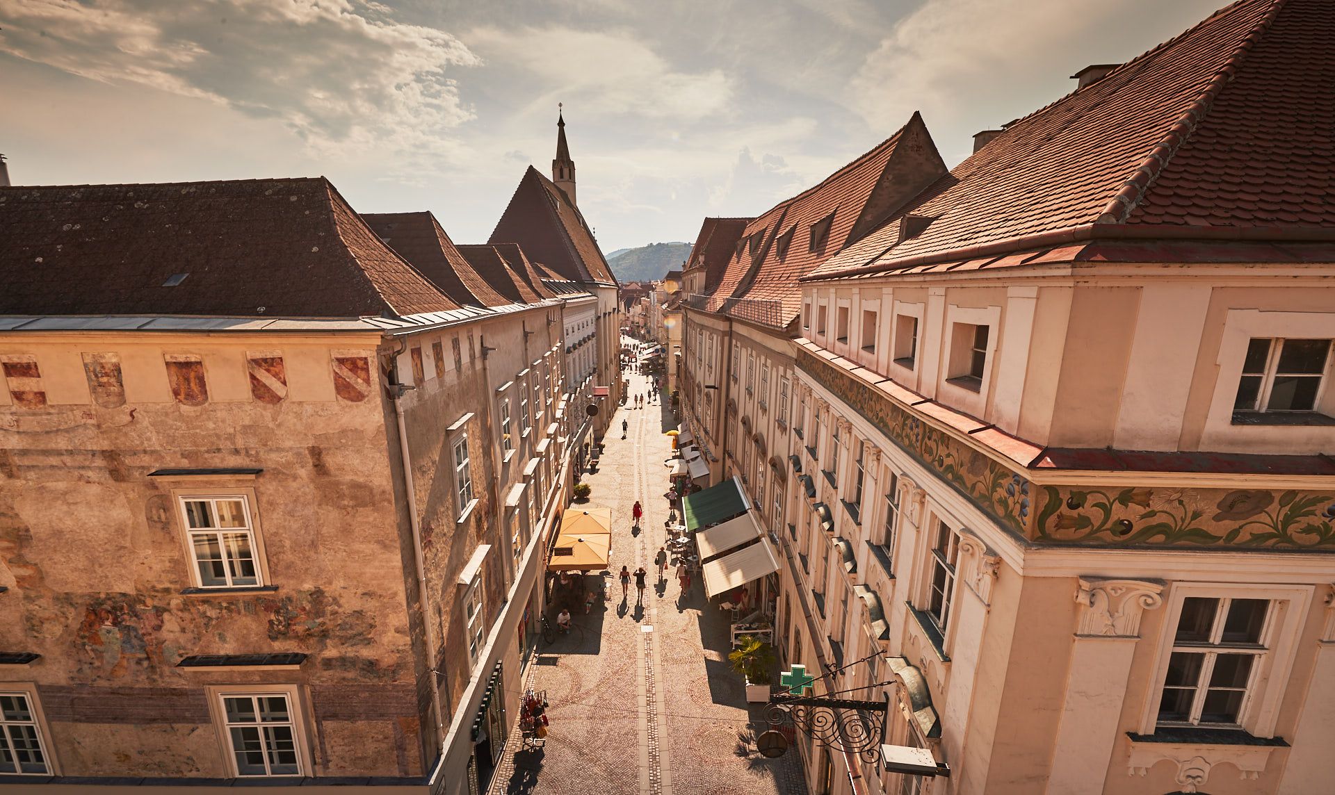 Blick auf eine historische Straße in der Altstadt von Krems mit alten Gebäuden und Menschen, die spazieren gehen.