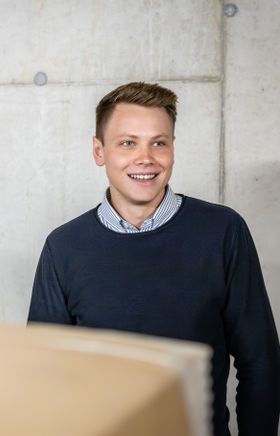 Junger Herr in dunklem Pullover vor einem beigen Hintergrund