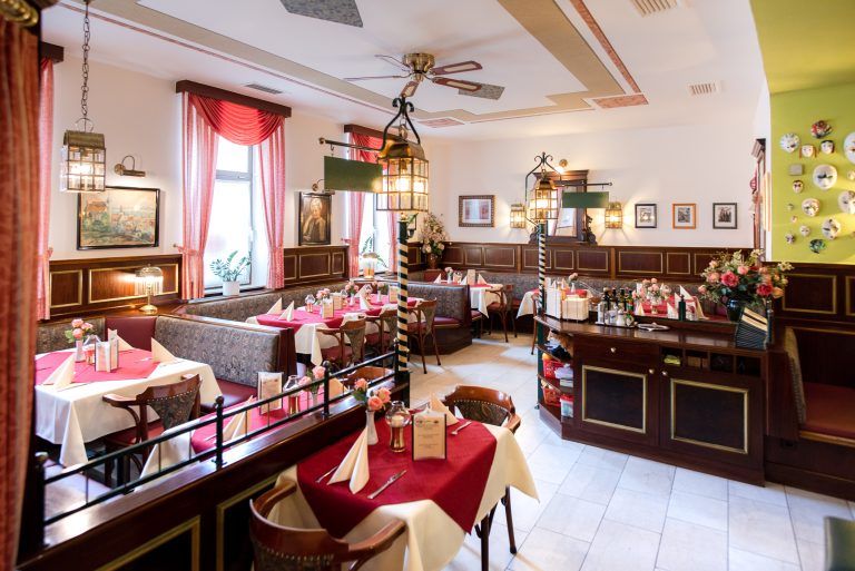 Innenansicht einer gemütlichen Pizzeria mit roten Tischdecken und dekorativen Lampen.