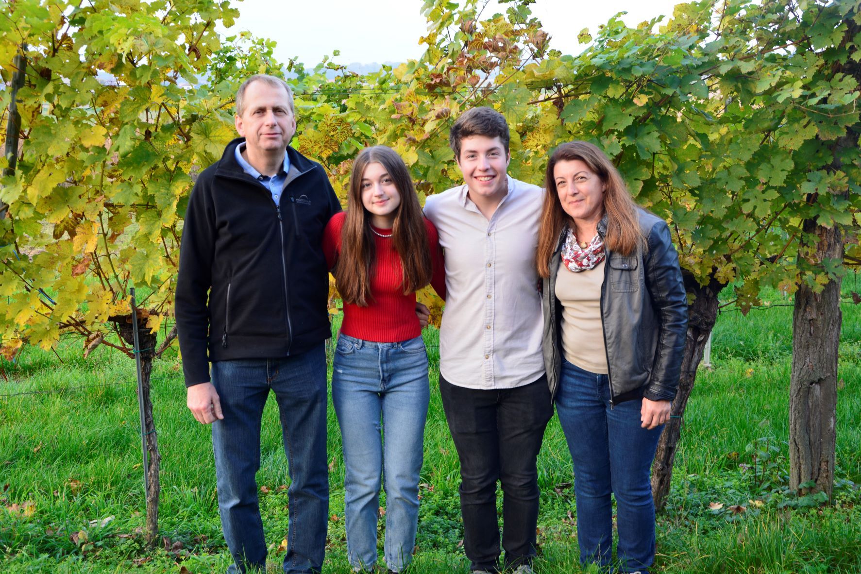 Vier Personen stehen lächelnd vor Weinreben im Freien.