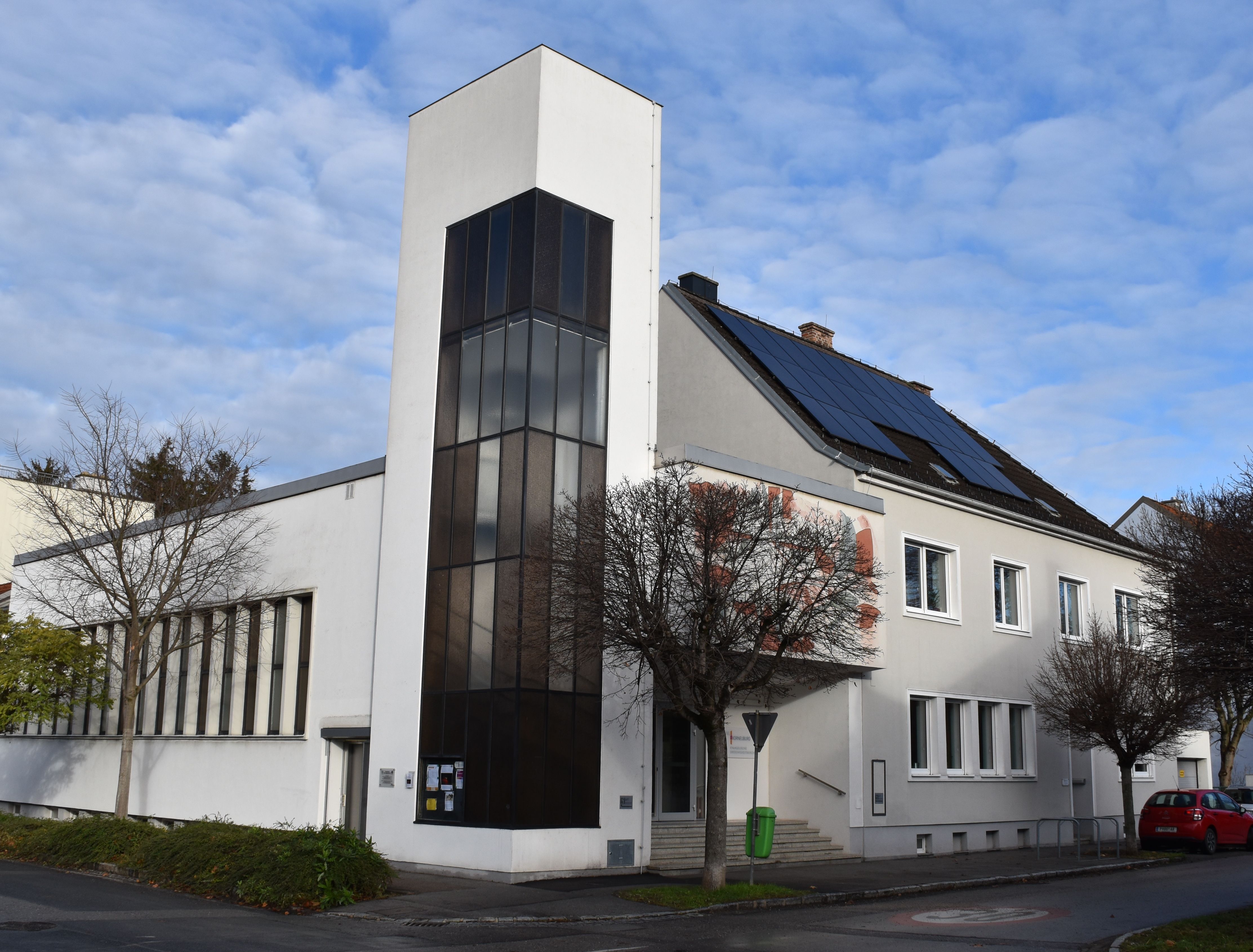 Moderne Kirche mit weißer Fassade und Solarpanelen auf dem Dach.