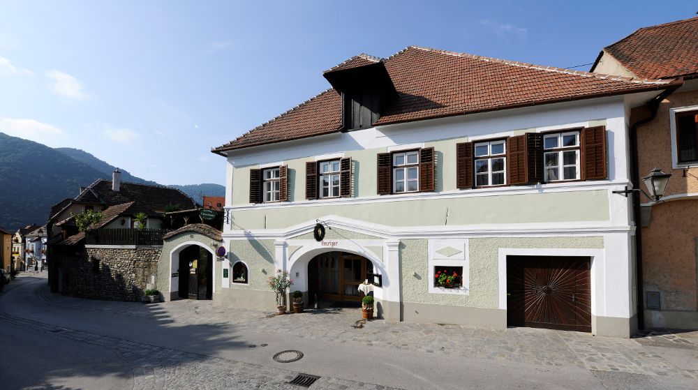 Traditionelles Haus mit grüner Fassade und braunen Fensterläden in einer ländlichen Umgebung.