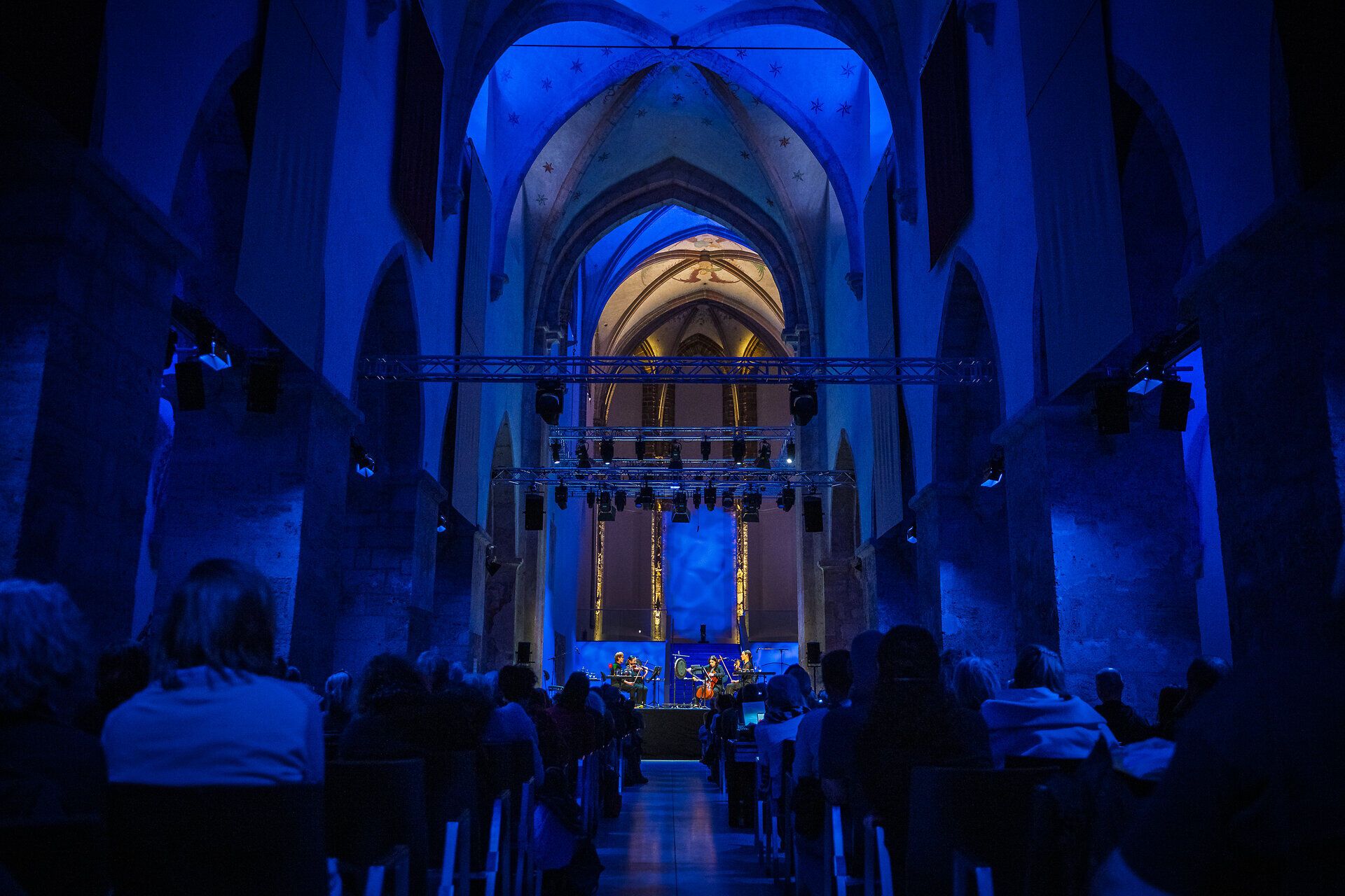 Publikum blickt in den blau beleuchteten Innenraum der Minoritenkirche Krems, wo Musiker:innen auf der Bühne des Klangraum Krems im Rahmen des Imago Dei Festivals auftreten.