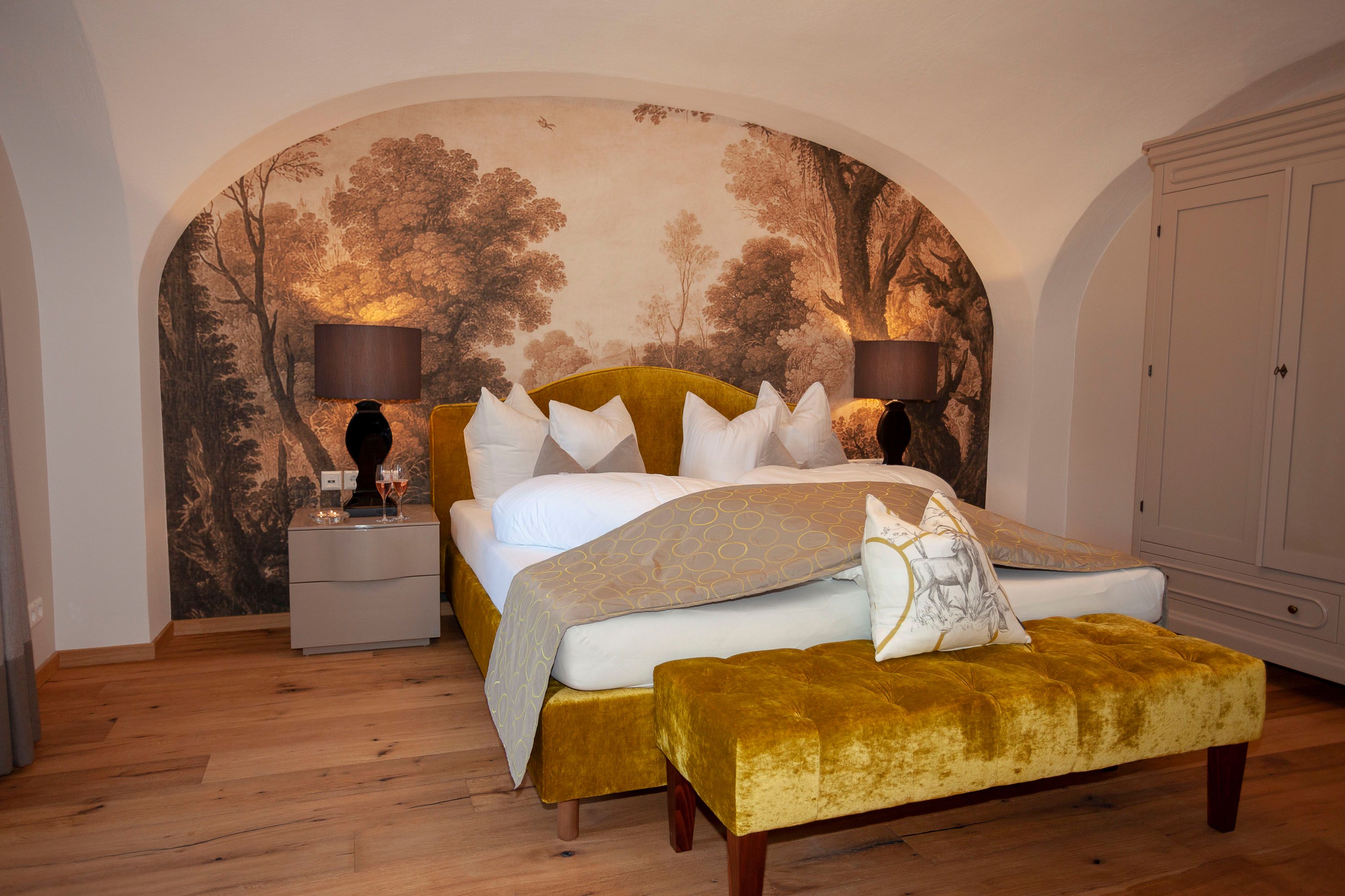 Elegante Suite mit gelbem Bett, Wandgemälde und Holzfußboden im Schloss Luberegg
