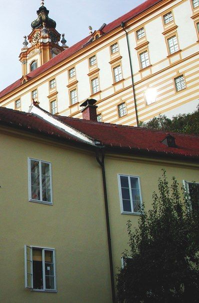 Gelbes Gebäude mit rotem Dach vor einem Kloster.