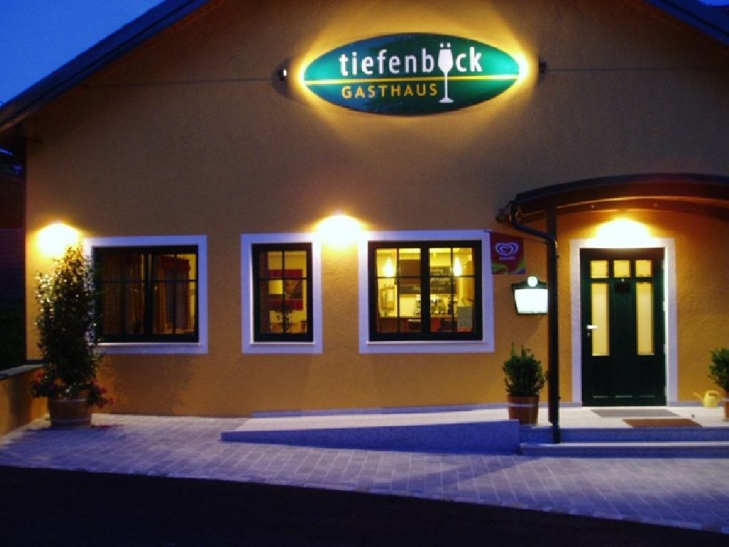 Außenansicht eines Gasthauses mit beleuchtetem Schild 'Tiefenböck'.