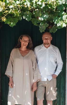 Ehepaar steht vor der grünen Eingangstüre, Weinblätter bilden ein Vordach über der Tür.