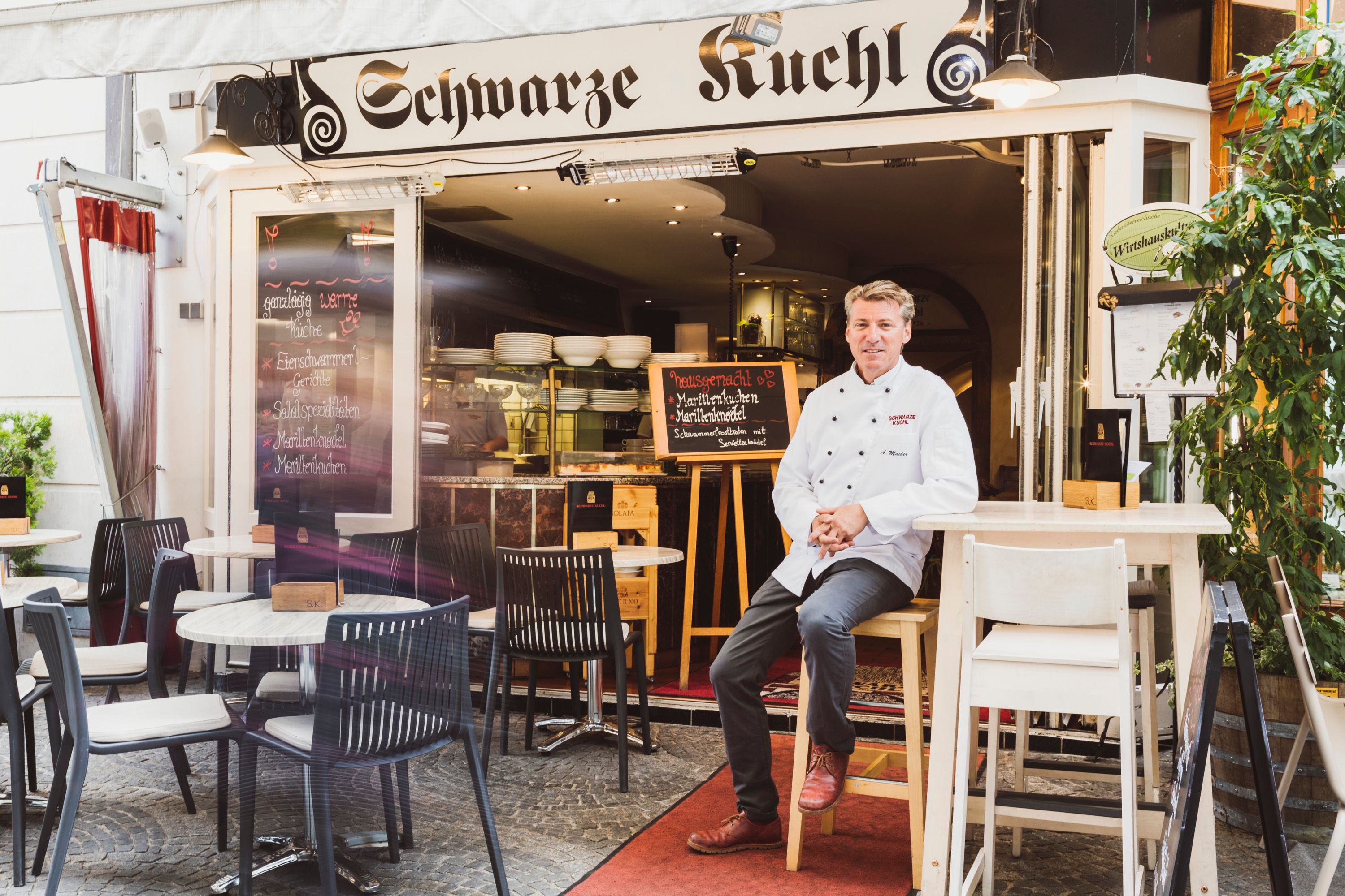 Restaurant 'Schwarze Kuchl' mit Koch vor dem Eingang, Tische im Freien.